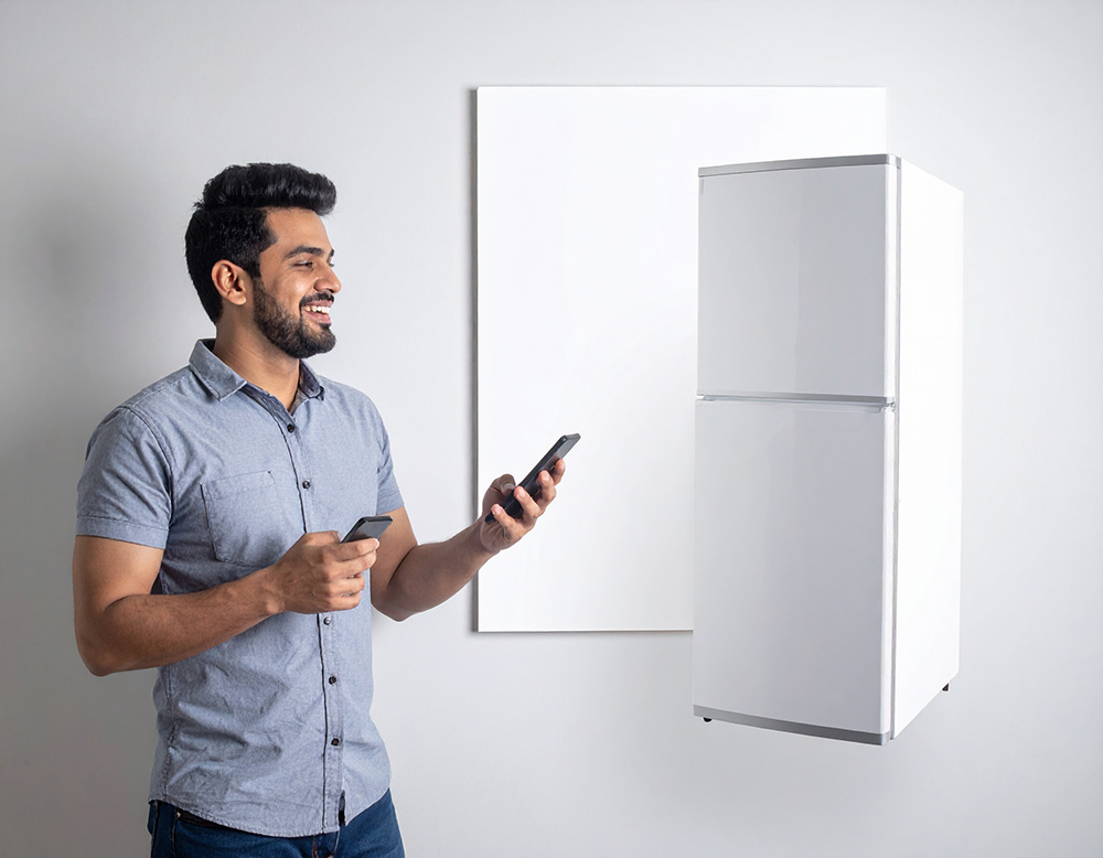 壁のポスターから冷蔵庫が浮かぶのを見ているスマートフォンを手にもって喜ぶ男性